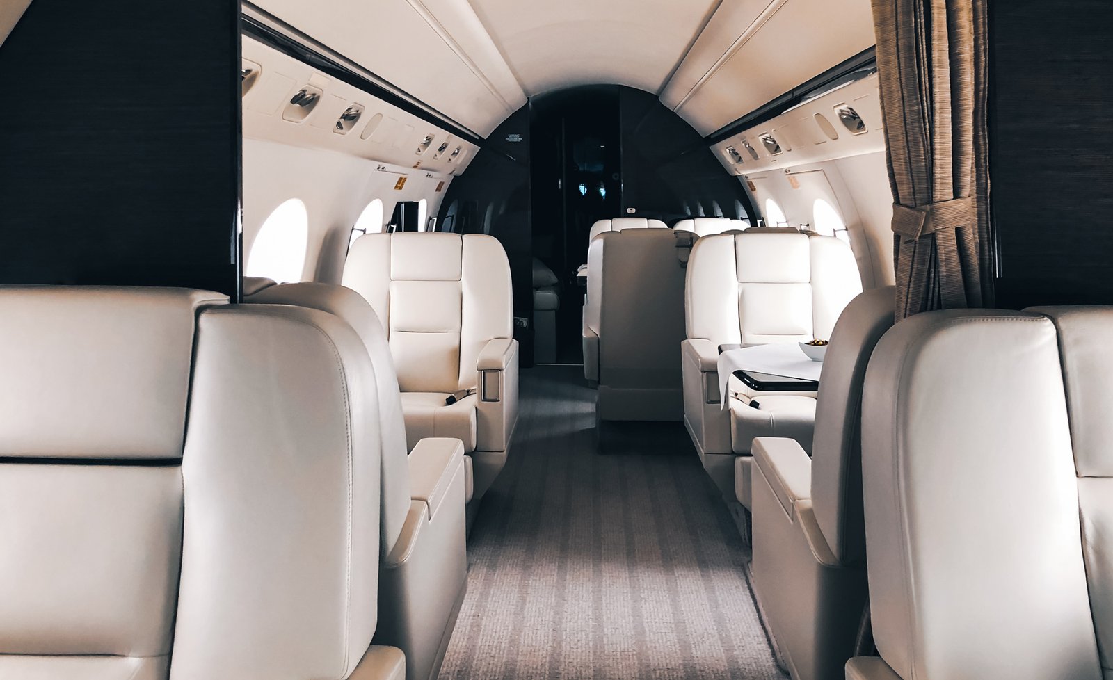 Light jet cabin looking aft down the aisle between cream leather club seats