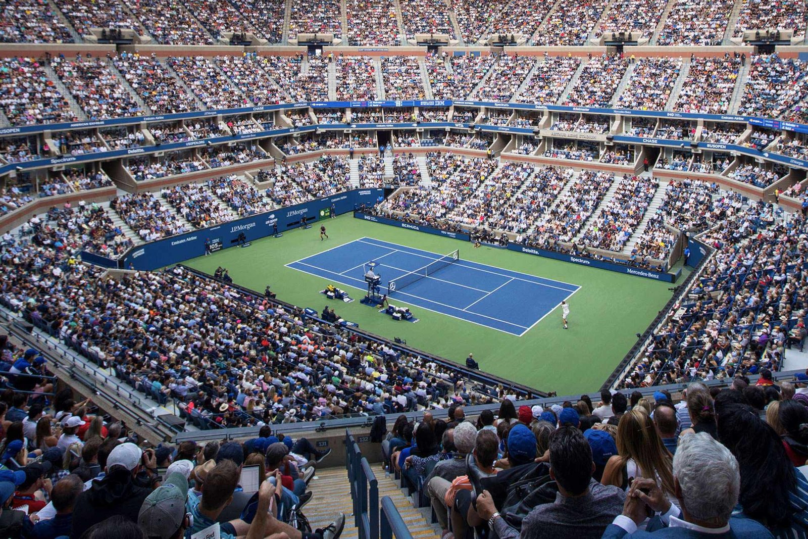 Packed tennis stadium under lights during a night match on the blue court